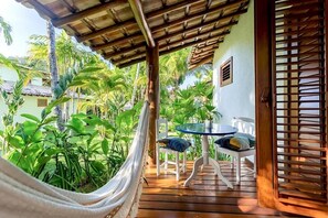 A wooden deck with a hammock, a round table with chairs, and lush greenery. - Paraíso Casa Branca (Arraial d'Ajuda)