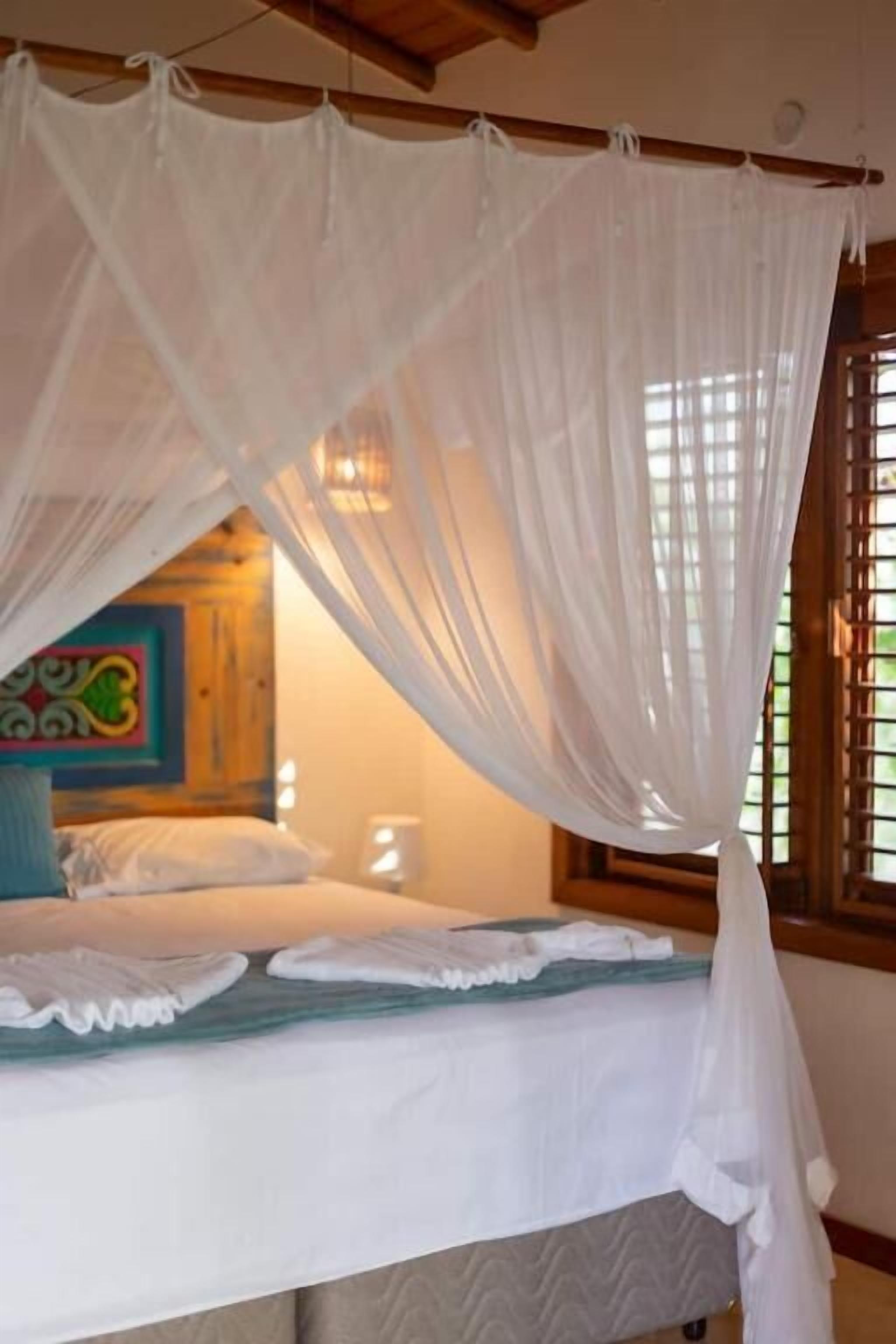A bed with a canopy, a pillow, a bedside table, and a window with bars.