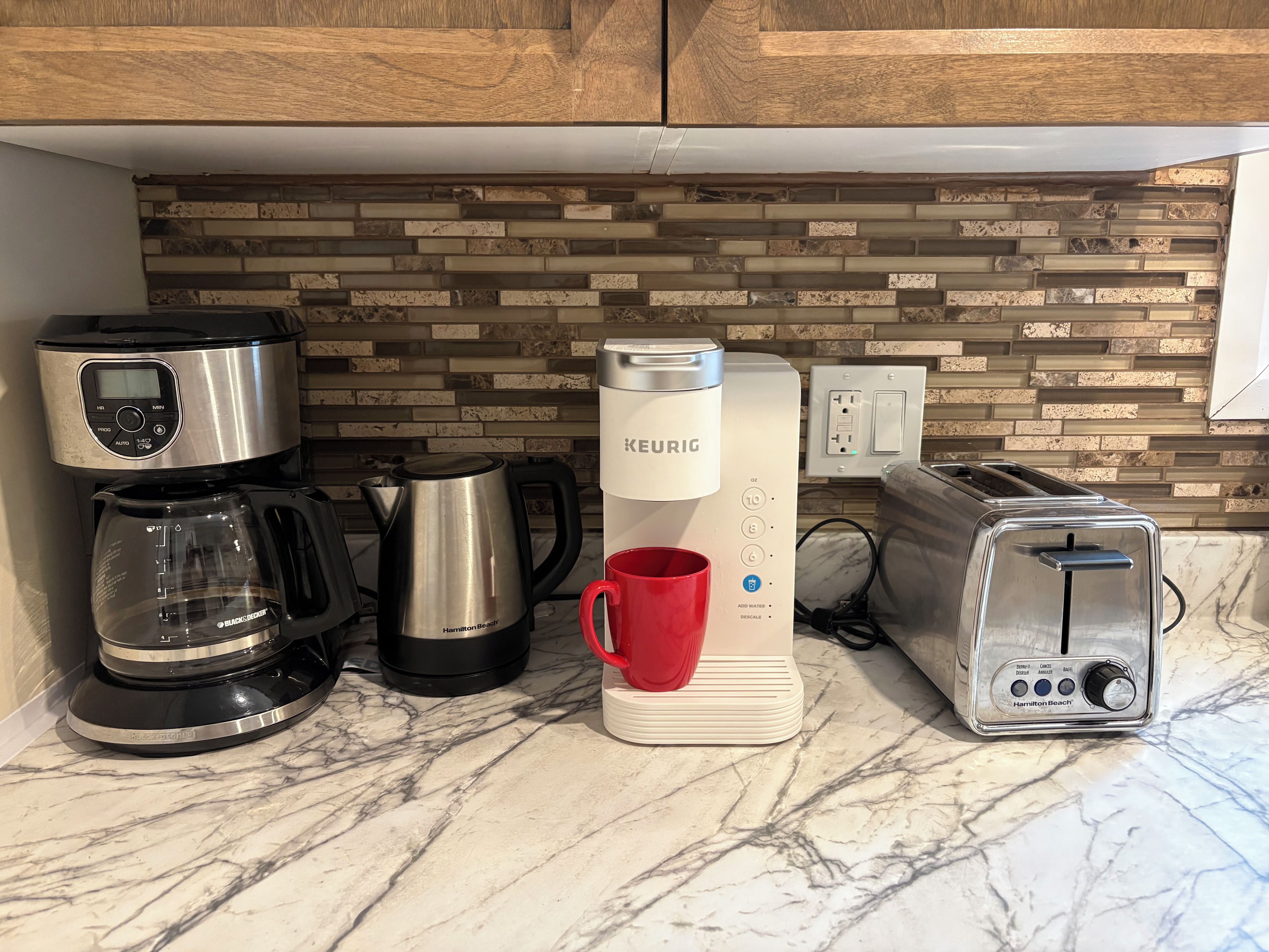 Una encimera de cocina con cafetera, hervidor, tostadora y taza.