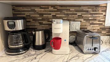 Una encimera de cocina con cafetera, hervidor, tostadora y taza.