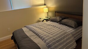 A bedroom with a bed, a nightstand, a lamp, and a window with blinds. - Two bedroom cozy apartment in central location, 15 minute from historic downtown (St. John's)