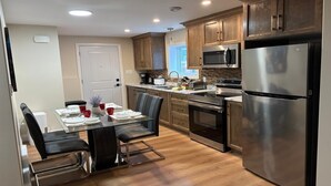A modern kitchen with wooden cabinets, stainless steel appliances, and a dining area with a glass table and chairs. - Two bedroom cozy apartment in central location, 15 minute from historic downtown (St. John's)