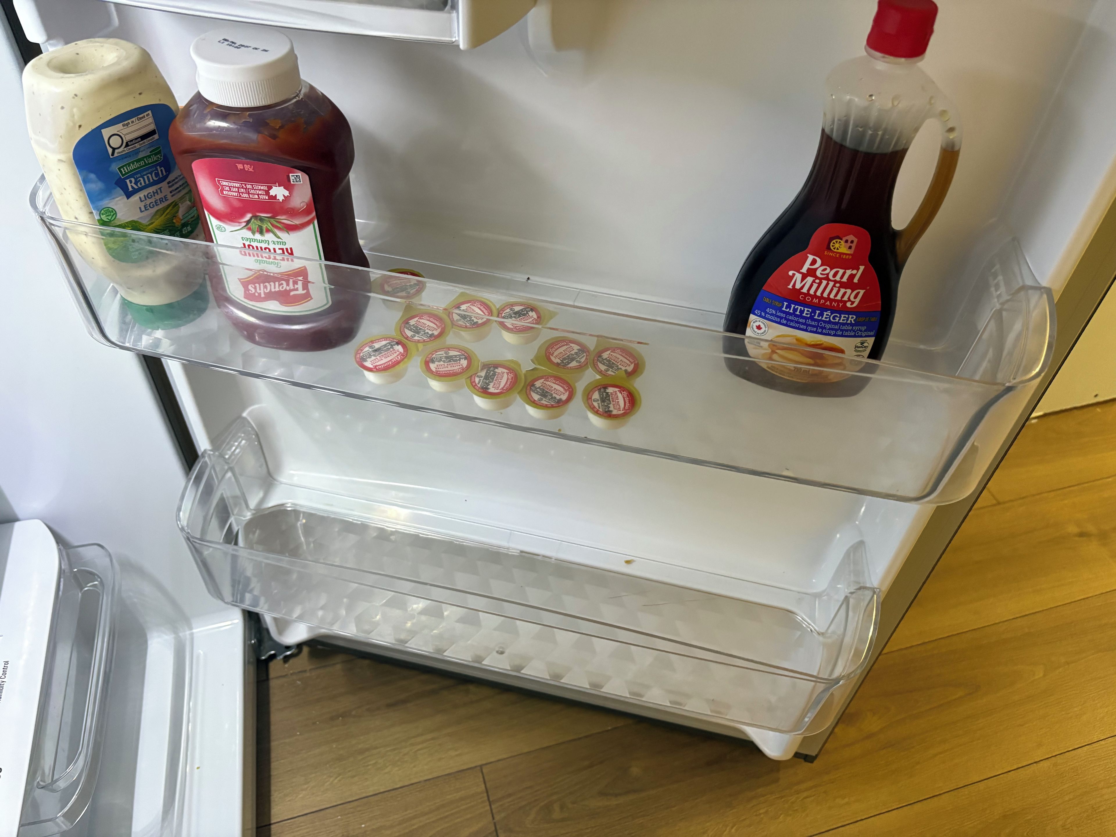 Un refrigerador con un estante transparente que contiene condimentos y una botella de leche.