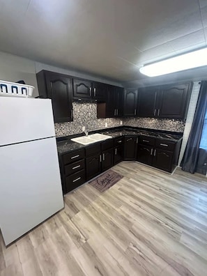 A kitchen with dark cabinets, a white refrigerator, a tiled backsplash, and a wooden floor.