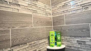 Douchegedeelte met een regendouche en een zwarte handdouche. Drie groene flessen staan op een witte plank.