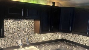 Una cucina moderna con mobili scuri, una parete rivestita di piastrelle e un lavello doppio.