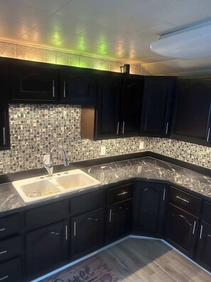 A modern kitchen with dark cabinetry, a tiled backsplash, and a double sink.