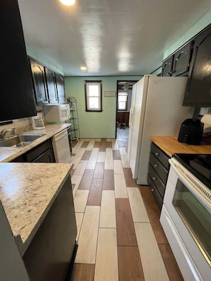 A compact kitchen with a microwave, stove, and cabinets. A window provides natural light, and the floor has a checkered tile pattern.