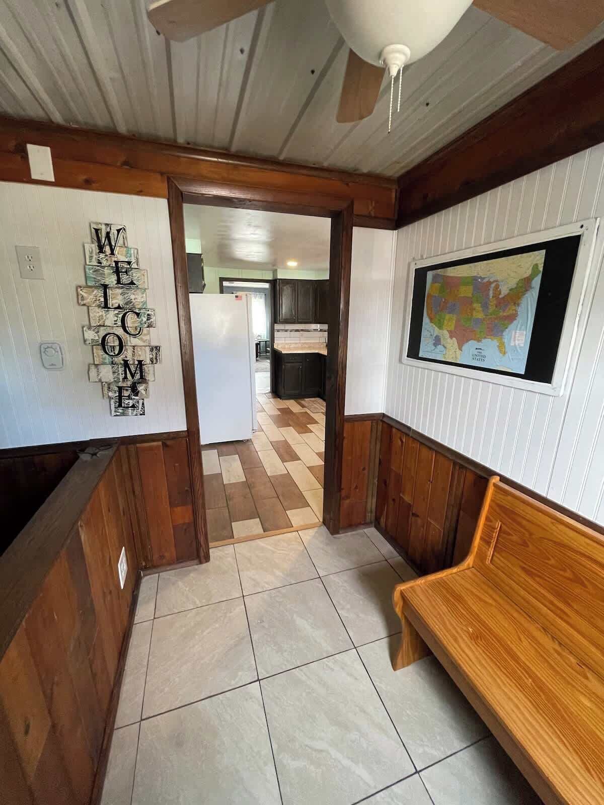 Un couloir avec une pancarte de bienvenue, une carte accrochée au mur et un banc en bois.