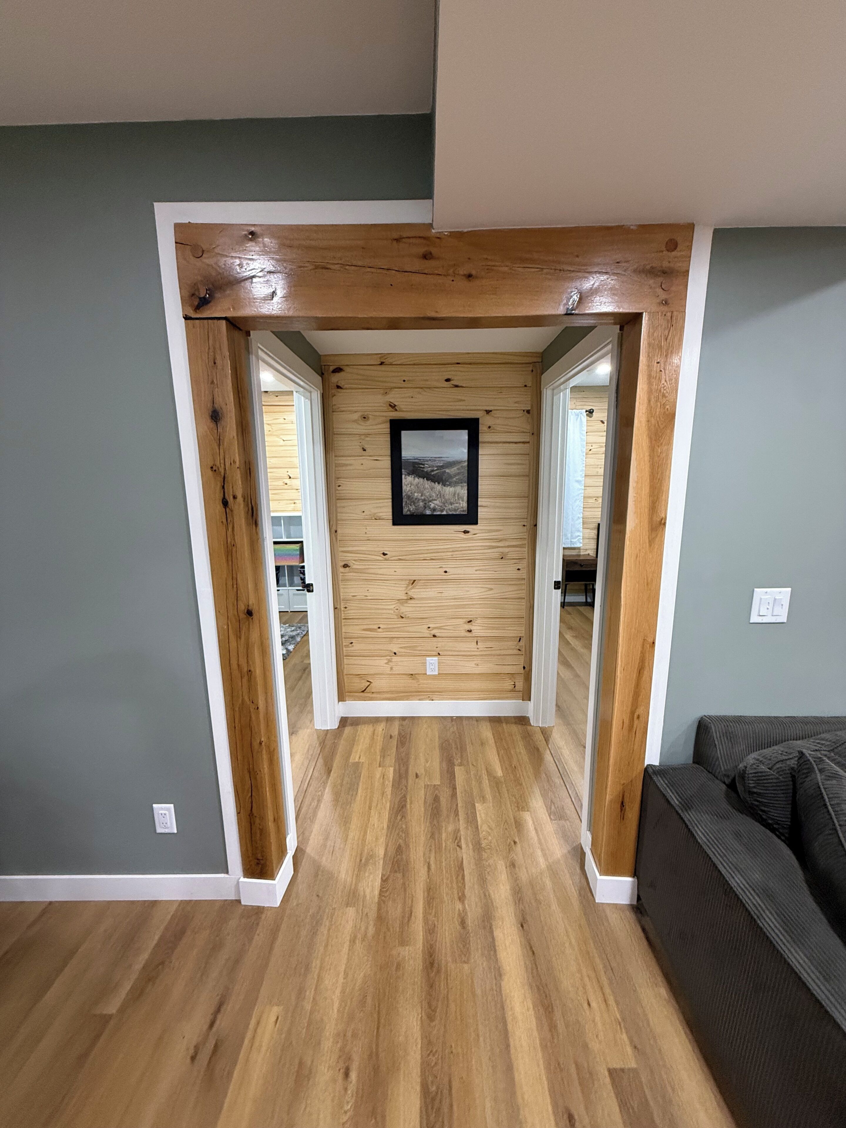 A hallway with wooden flooring, a framed picture on the wall, and a couch in the foreground.