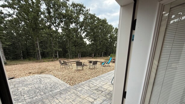 An outdoor patio with stone flooring, a seating area with chairs, and a view of a forested area. - 6BR Ozark Retreat on 10 Private Acres - Fire Pits, Game Room & Patio (Saint James)