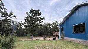 A blue building with a deck and a large tree in the yard. - 6BR Ozark Retreat on 10 Private Acres - Fire Pits, Game Room & Patio (Saint James)