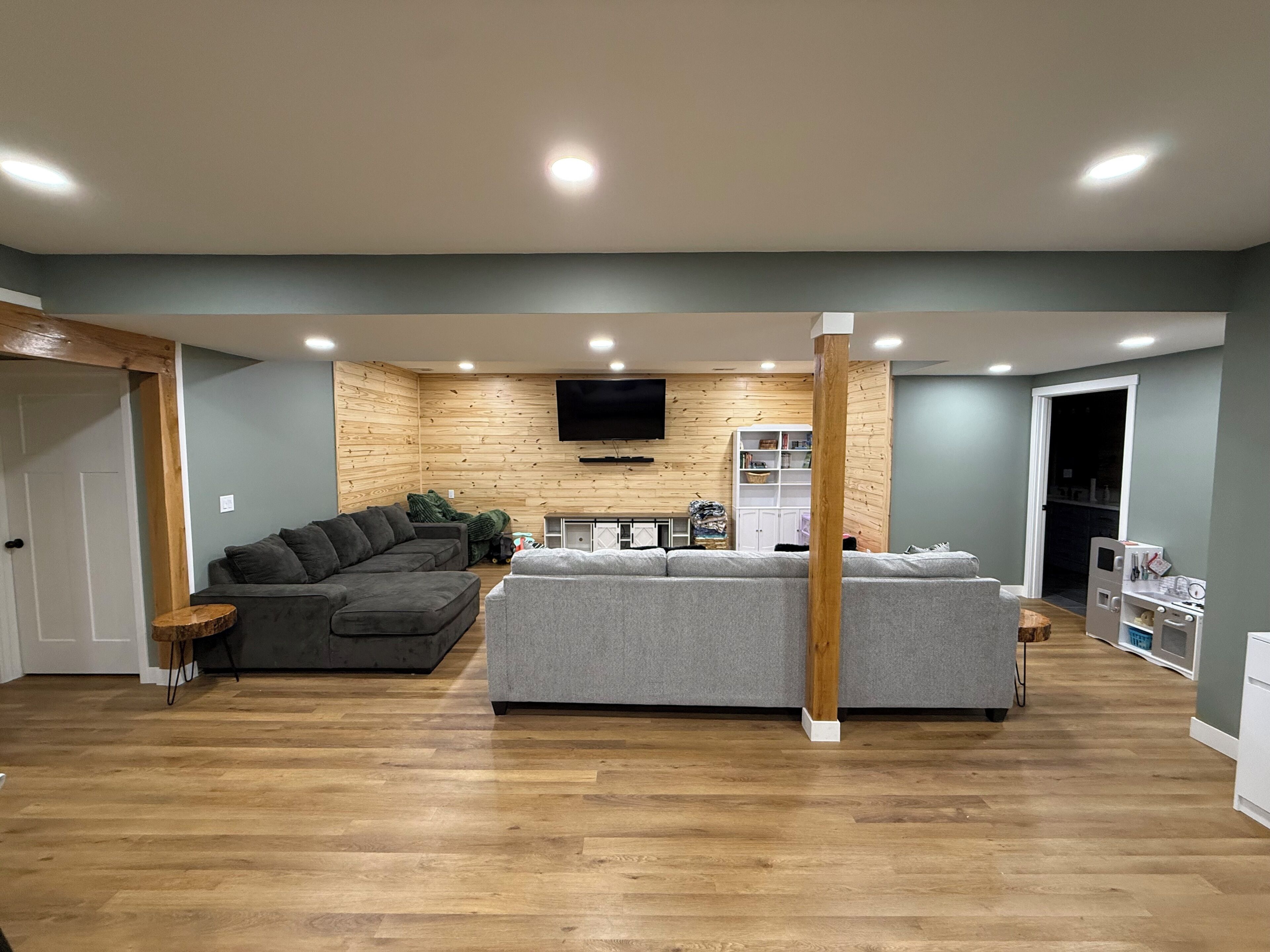 A living room with a grey sofa, a wooden accent wall, and a flat-screen TV mounted above.