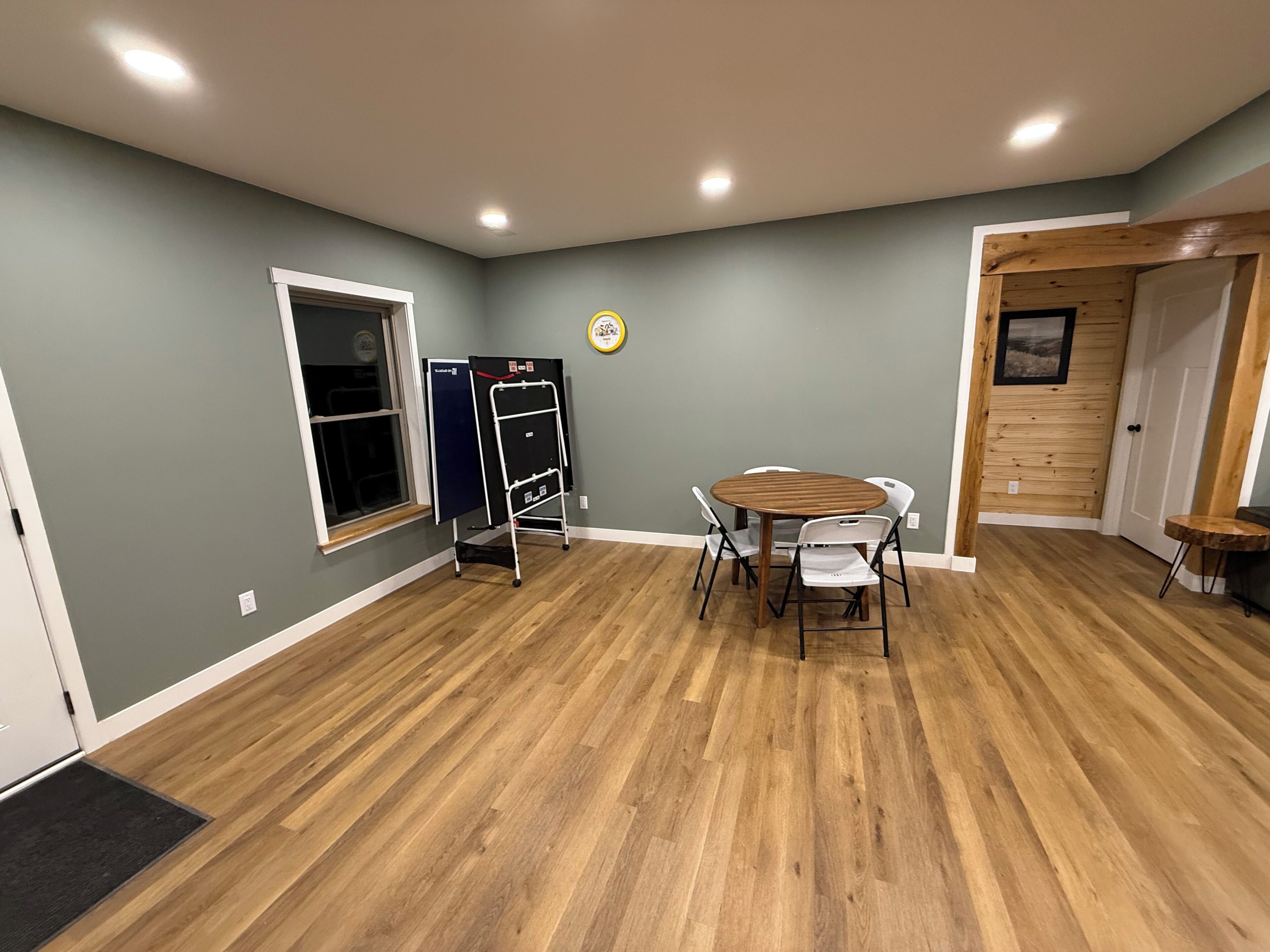 Una habitación con piso de madera, una mesa redonda con sillas, una pizarra y una puerta con panel de madera.