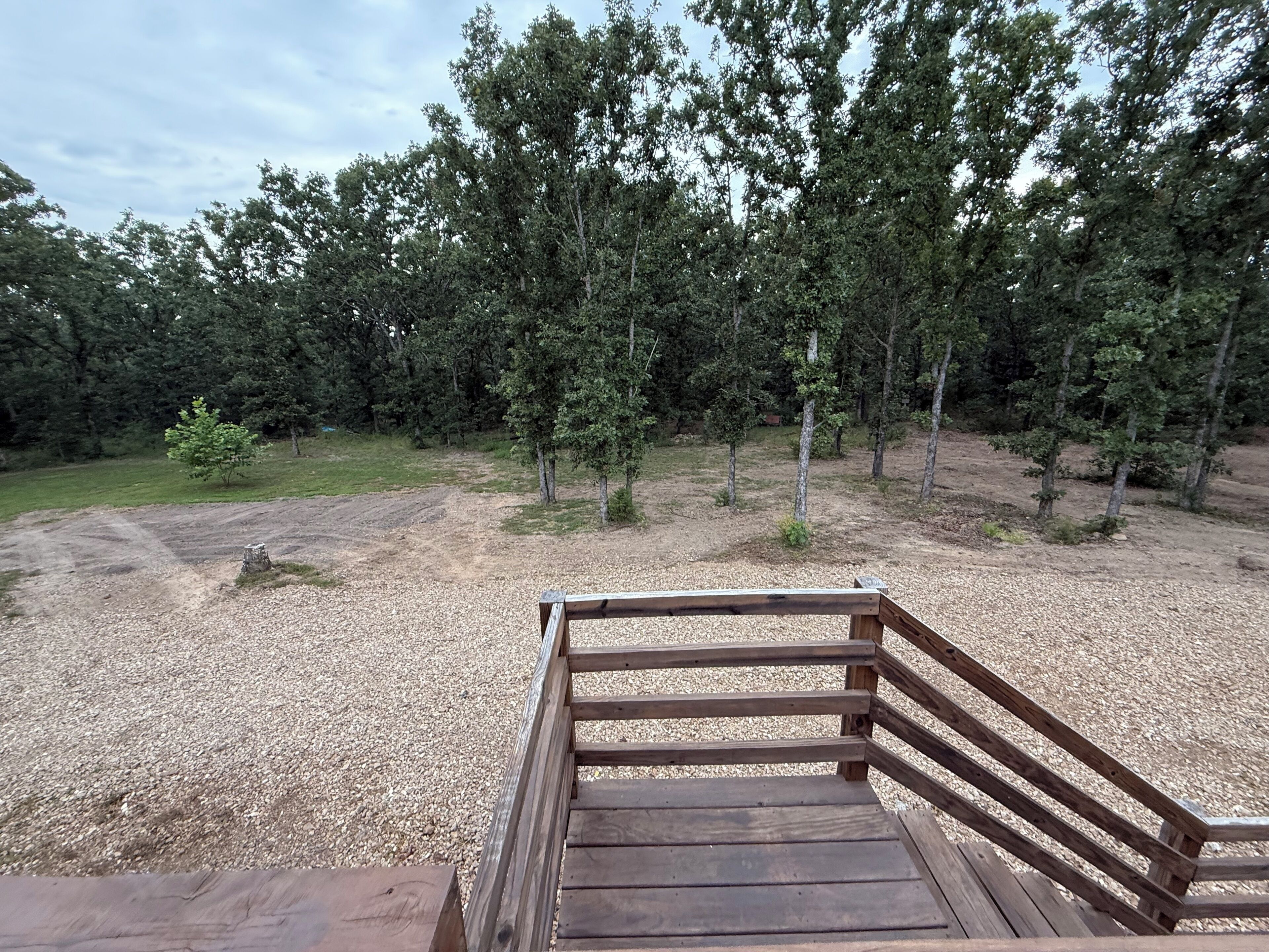 A wooden deck with a gravel path leading to a forested area.