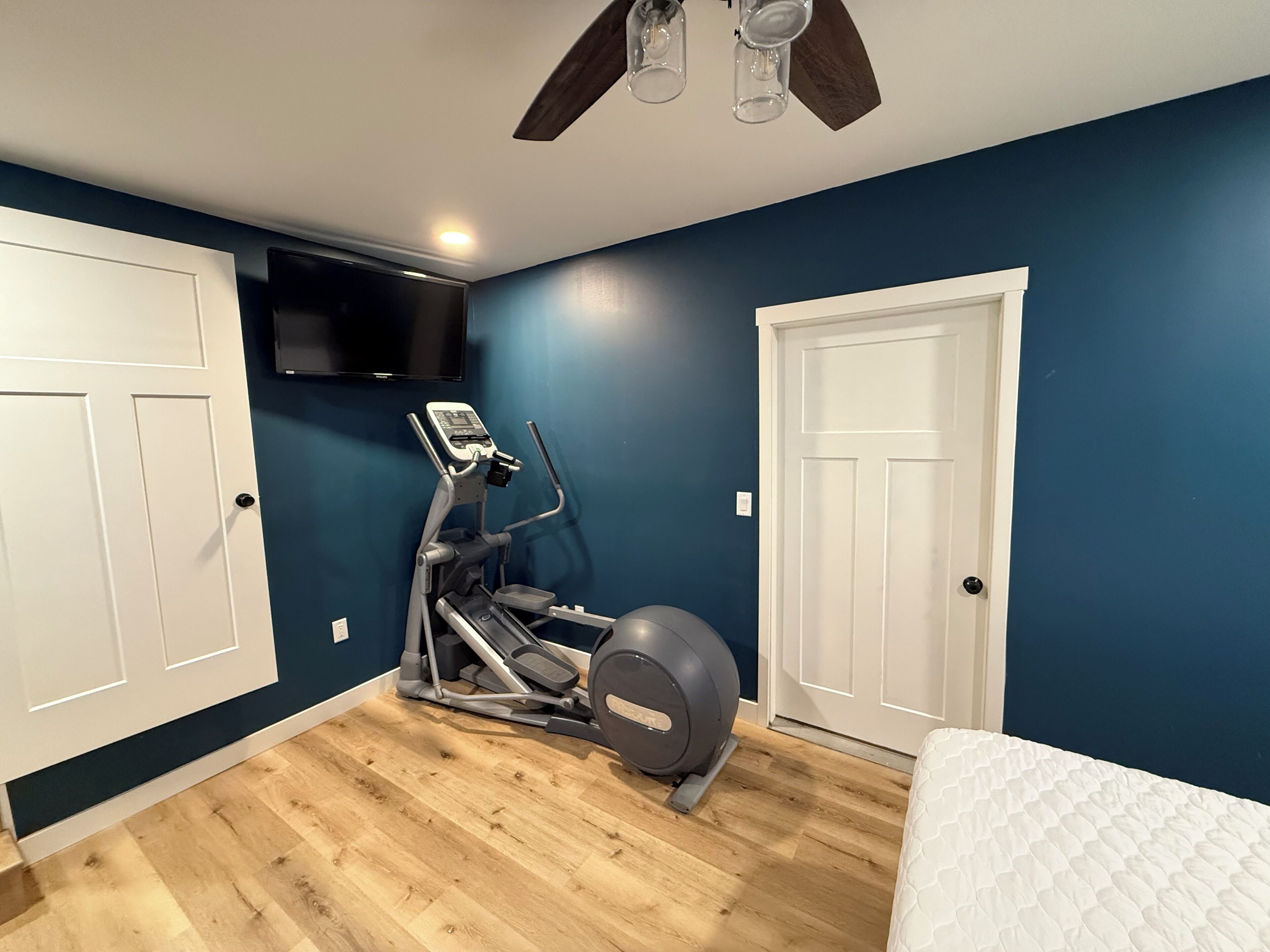 Una habitación con ventilador de techo, cinta de correr y televisor montado en la pared.