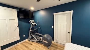 Una habitación con ventilador de techo, cinta de correr y televisor montado en la pared.
