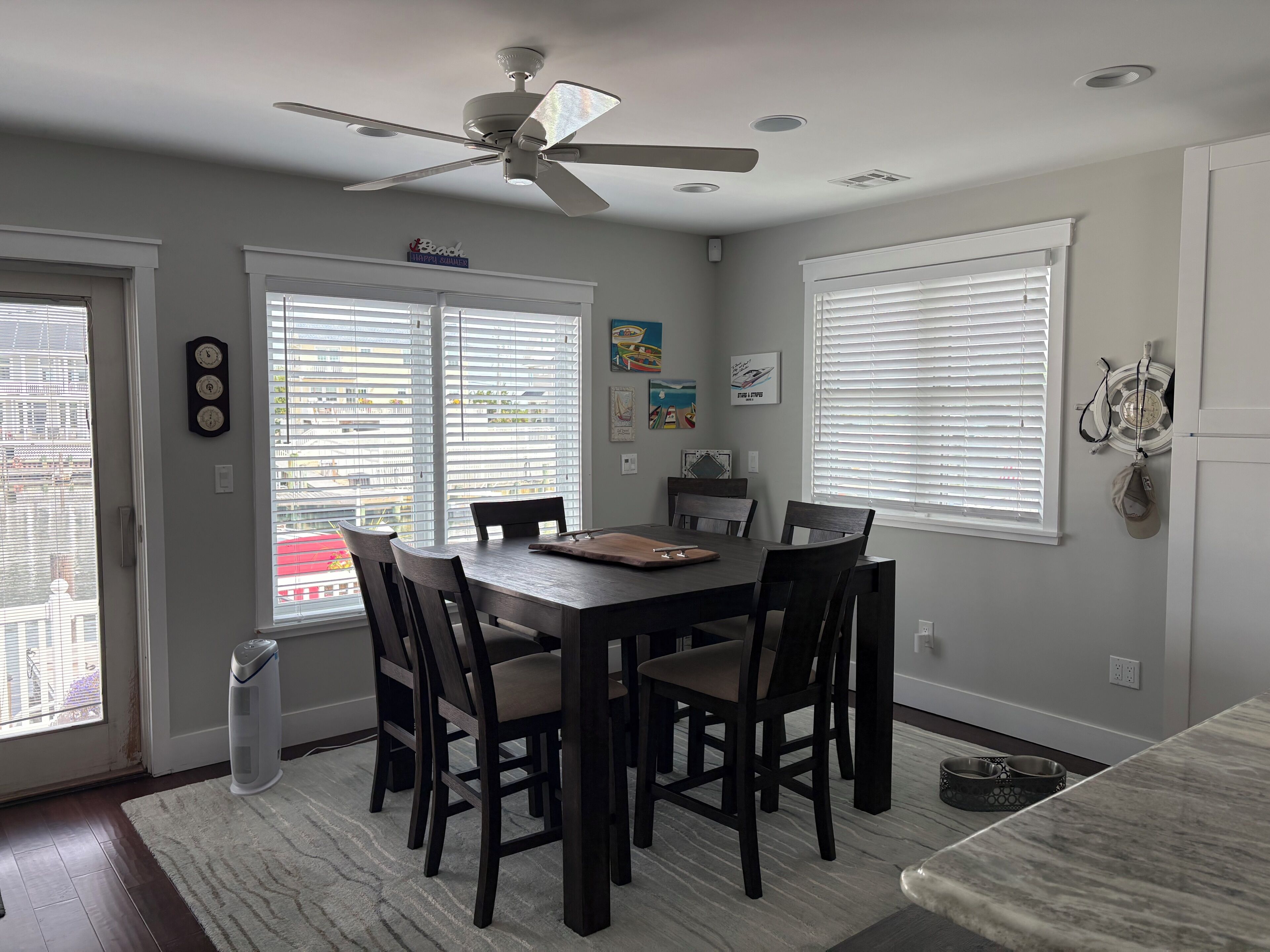 A dining area with a table, chairs, a ceiling fan, and windows with blinds.