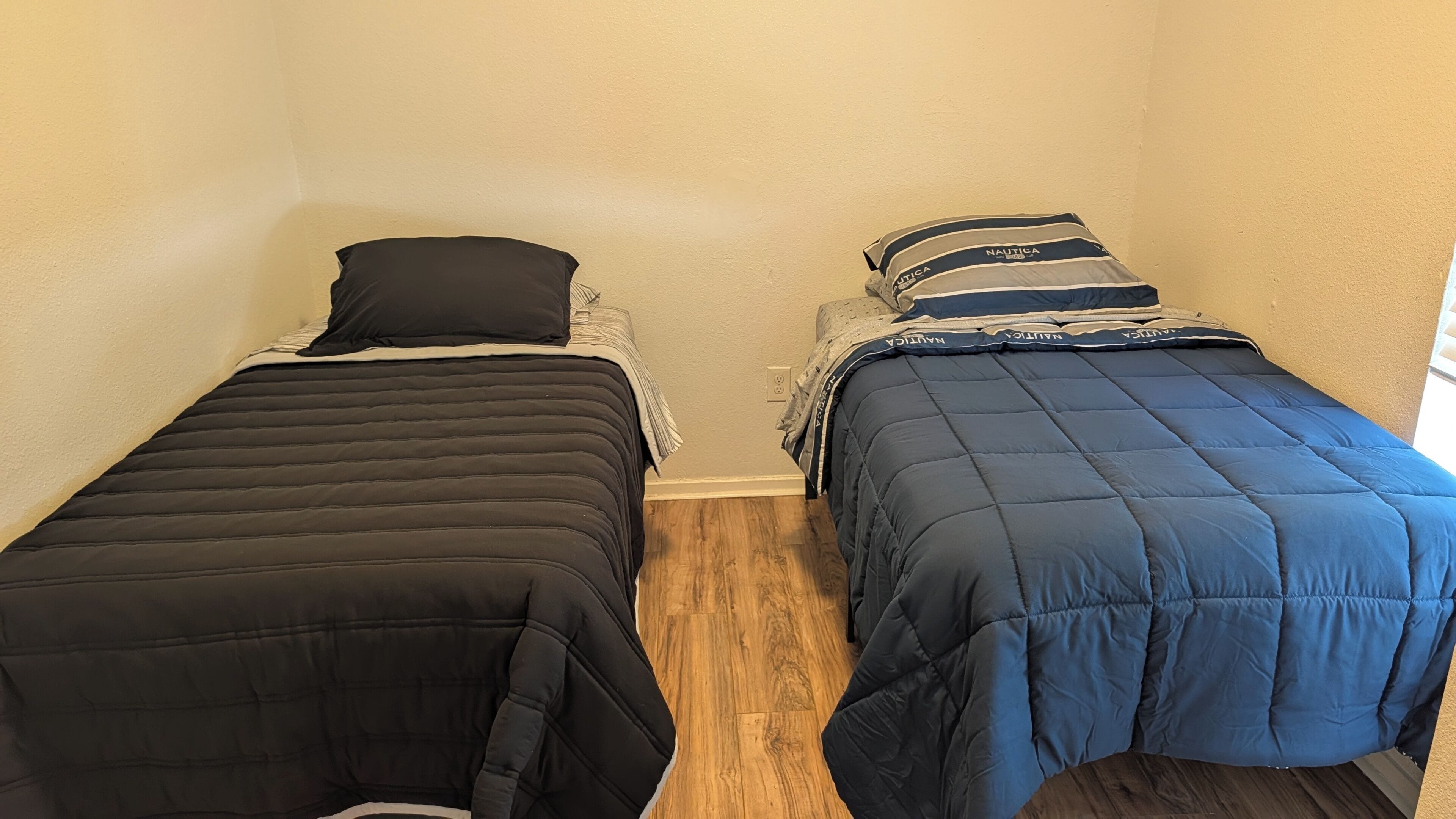 Zwei Einzelbetten mit schwarzer und blauer Bettwäsche, ein Holzboden und eine schlichte Wand.