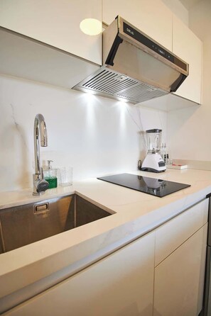 Eine moderne Küche mit Spüle aus Edelstahl, integrierter Dunstabzugshaube und Arbeitsplatte mit Mixer.