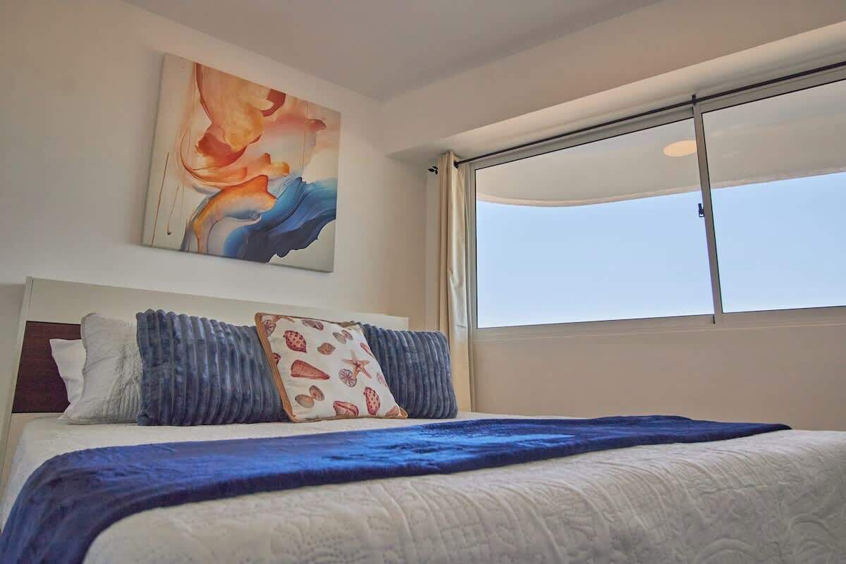 Habitación de hotel con una cama grande, una ventana con cortinas y un cuadro abstracto colgado en la pared.
