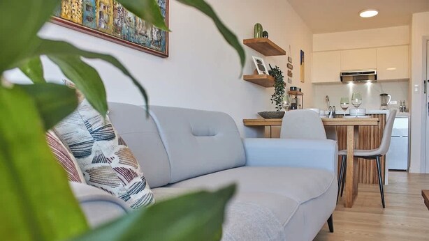 A modern living room with a sofa, a dining table, and a kitchen area in the background. - Refugio en el Mar Despierta frente al Caribe (Porlamar)