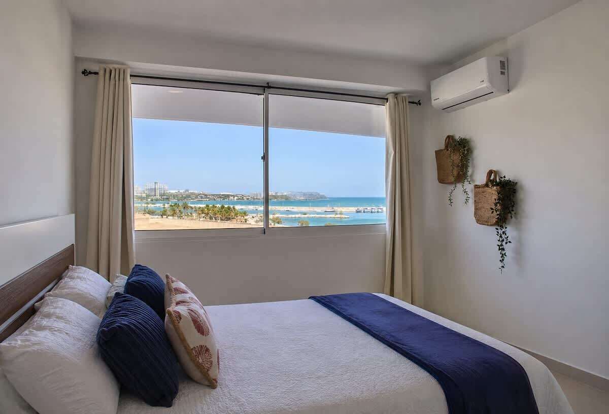 Ett hotellrum med en säng, utsikt över havet och en luftkonditioneringsanläggning.