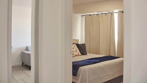 A bedroom with a bed, a bedside table, and a window with curtains. - Refugio en el Mar Despierta frente al Caribe (Porlamar)