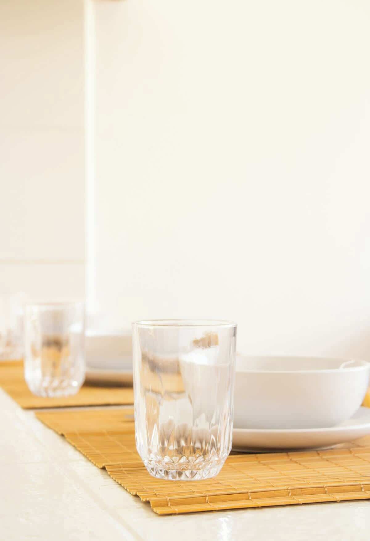 Un vaso transparente sobre un tapete de bambú, con un plato blanco al fondo.