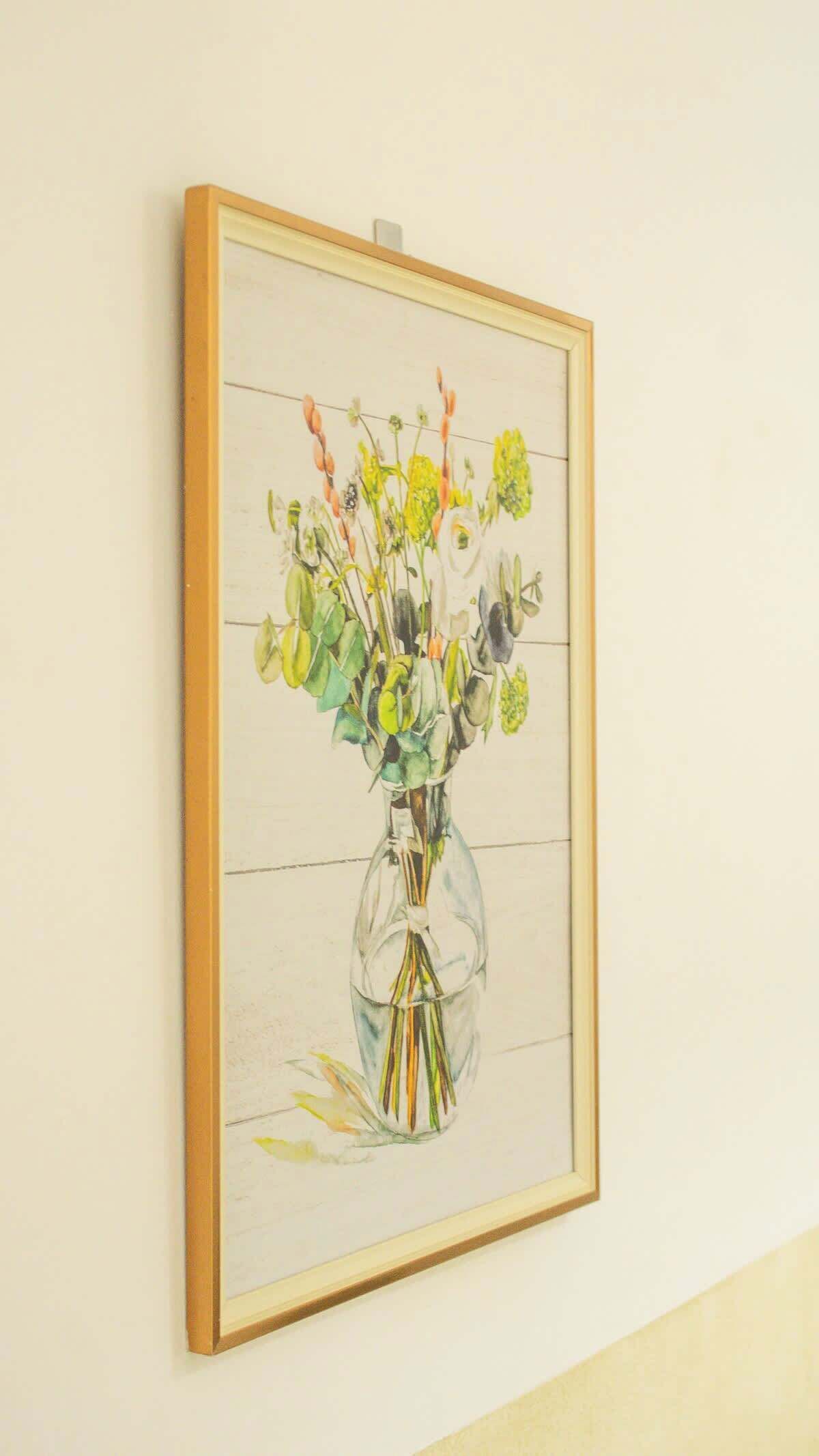 A framed artwork of a vase with flowers on a wall.