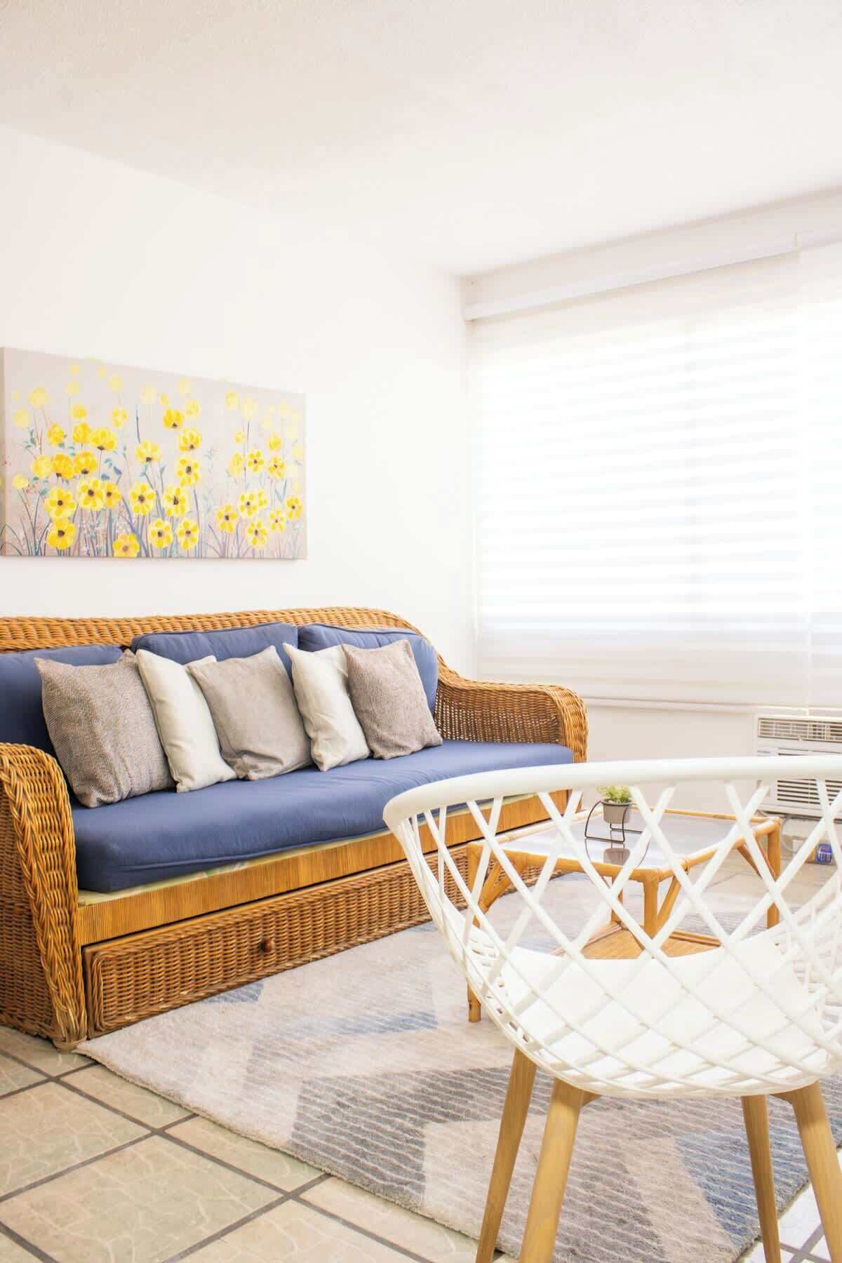 Ein Zimmer mit einem blauen Sofa, einem weißen Sessel und einem Gemälde mit gelben Blumen an der Wand.
