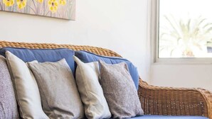 En fletsofa med blå puder og flere hynder, placeret i et rum med et stort vindue og et blomsterbillede på væggen.
