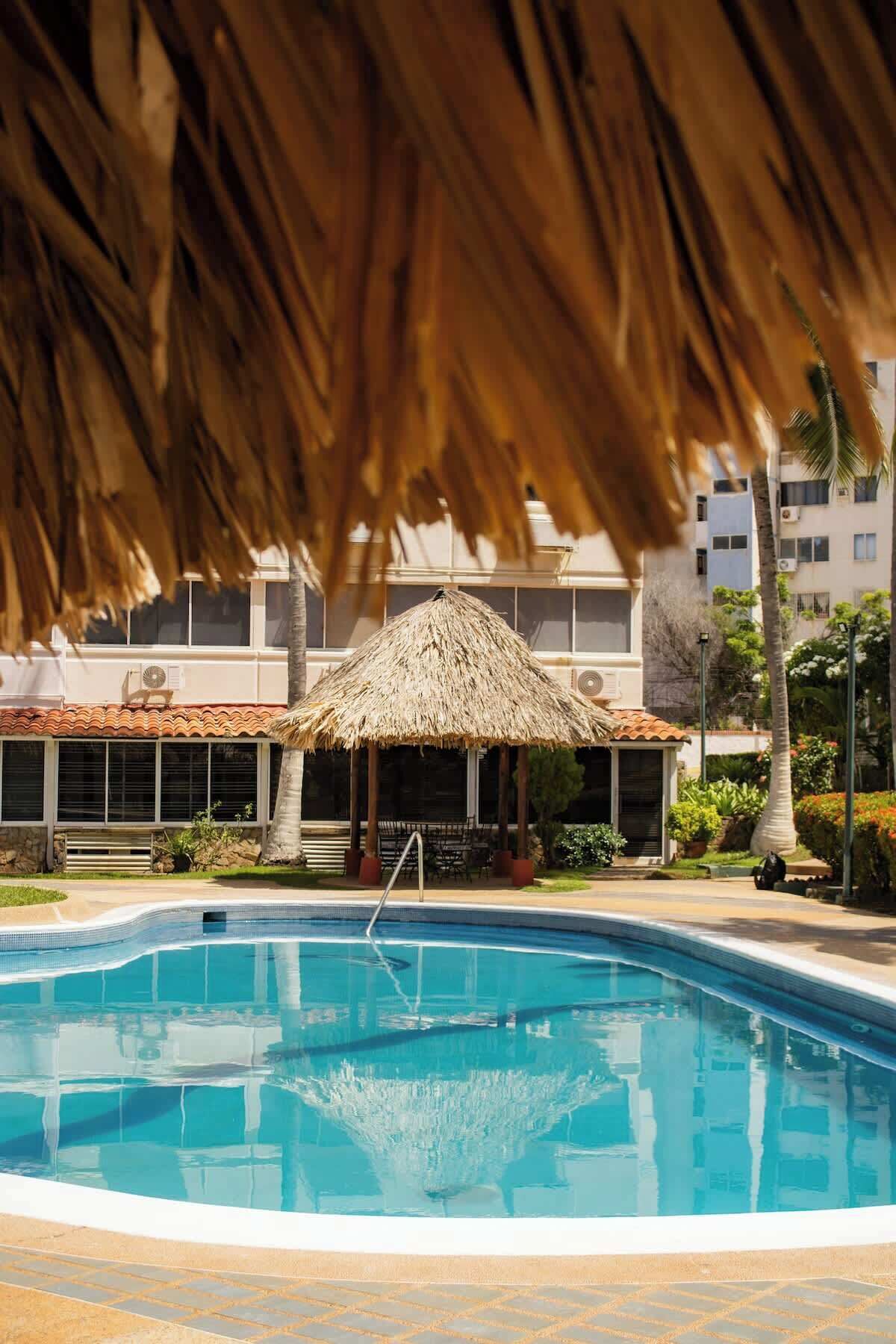 Una piscina con una estructura de techo de paja y un edificio al fondo.