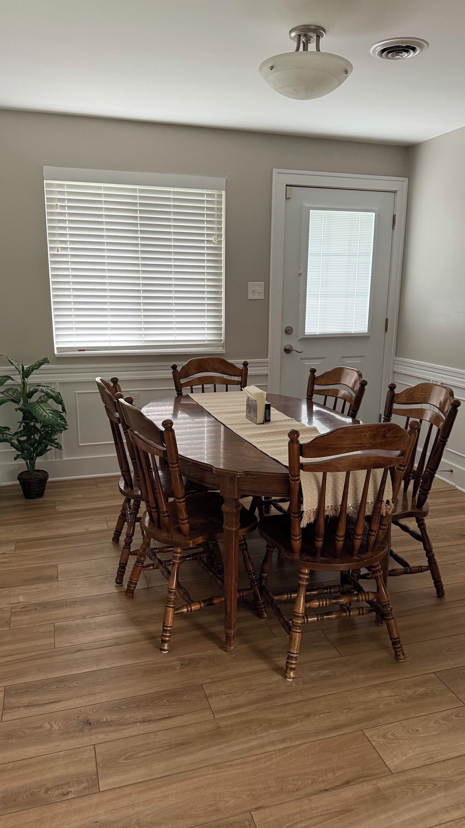 Un comedor con mesa y sillas de madera, una planta en maceta y una puerta con ventanal.