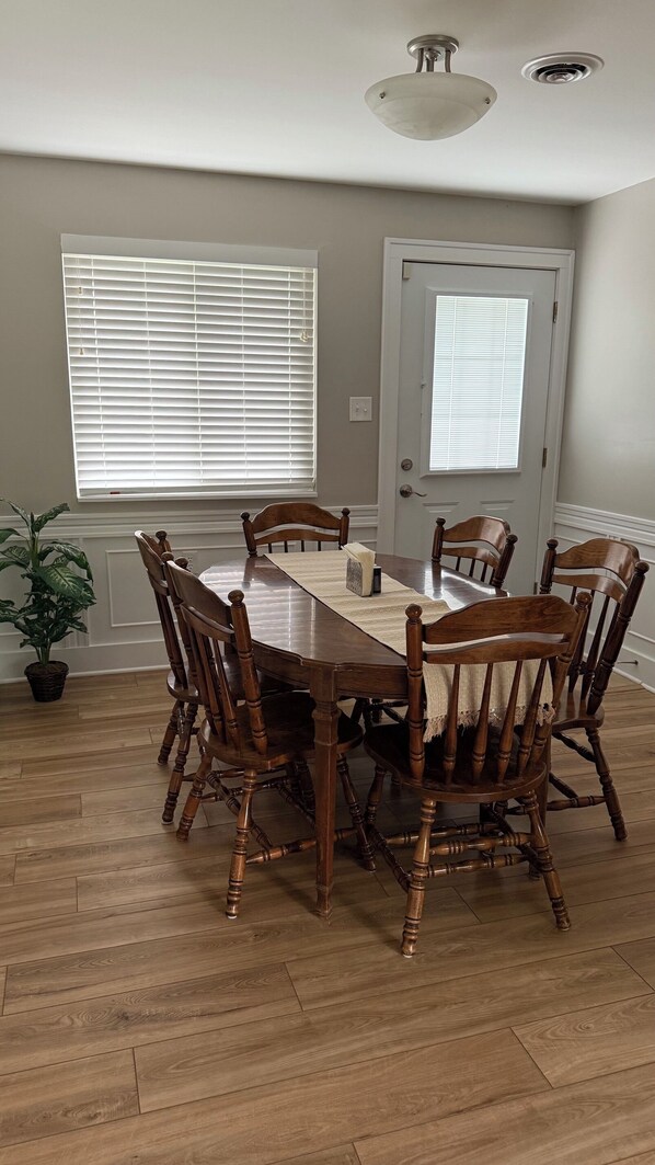 A dining room with a wooden table and chairs, a potted plant, and a door with a window.