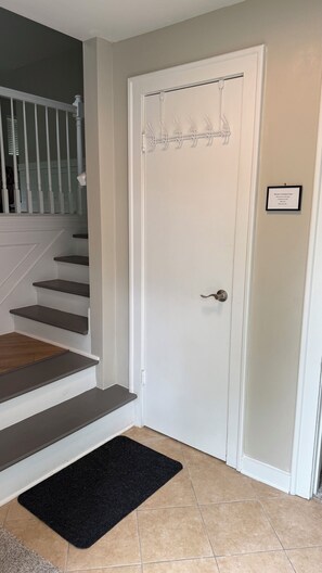 A white door with a coat rack, a black doormat, and a staircase with dark steps.