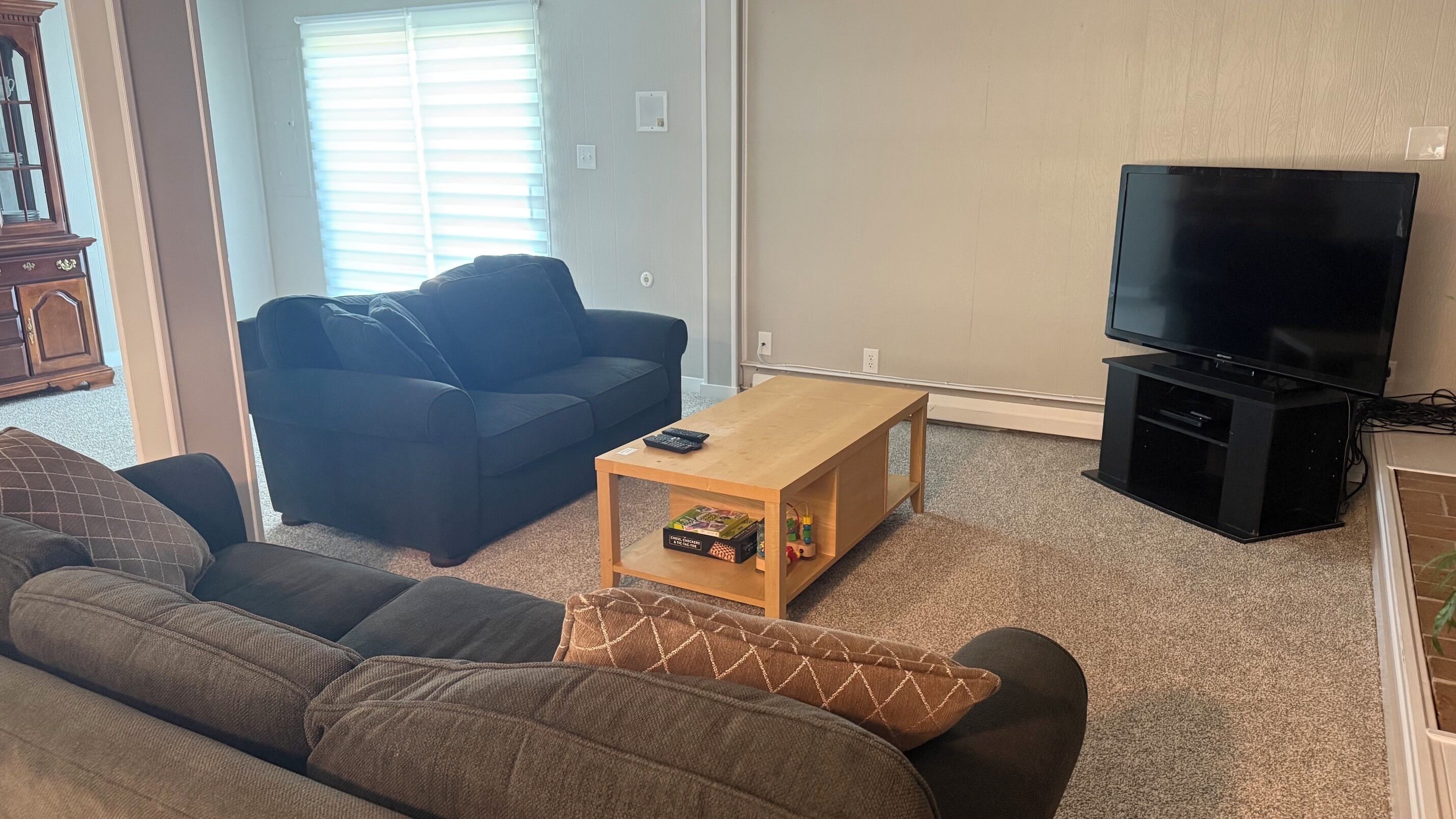 A living room with a sofa, a coffee table, a television, and a window with blinds.