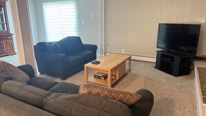 A living room with a sofa, a coffee table, a television, and a window with blinds.