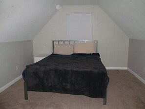 Ein kleines Zimmer mit einem Einzelbett, schrägen Wänden und einem Fenster mit Jalousien.