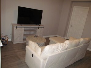 Ein Wohnzimmer mit einem weißen Sofa, einem Fernseher auf einem Holzboden und einer Tür im Hintergrund.