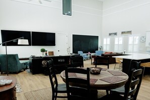 A modern living room with a dining area, a blackboard, and a large window. - The Endzone | 6BR Near UF & Shands Sleeps 14 (Gainesville)