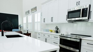 Uma cozinha moderna com armários brancos, forno de aço inoxidável, micro-ondas e pia.