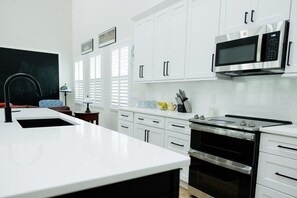A modern kitchen with white cabinets, a stainless steel oven, a microwave, and a sink. - The Endzone | 6BR Near UF & Shands Sleeps 14 (Gainesville)