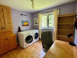 A laundry room with a washing machine, a chair, wooden cabinets, and a window with curtains.