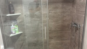 A glass-enclosed shower stall with a handheld showerhead, a shelf with toiletries, and a visible drain. - Well-located apartment (Platja de l'Arenal)