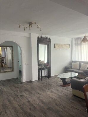 Ein Wohnzimmer mit einer Couch, einem runden Couchtisch, einem Spiegel und einer dekorativen Deckenleuchte.