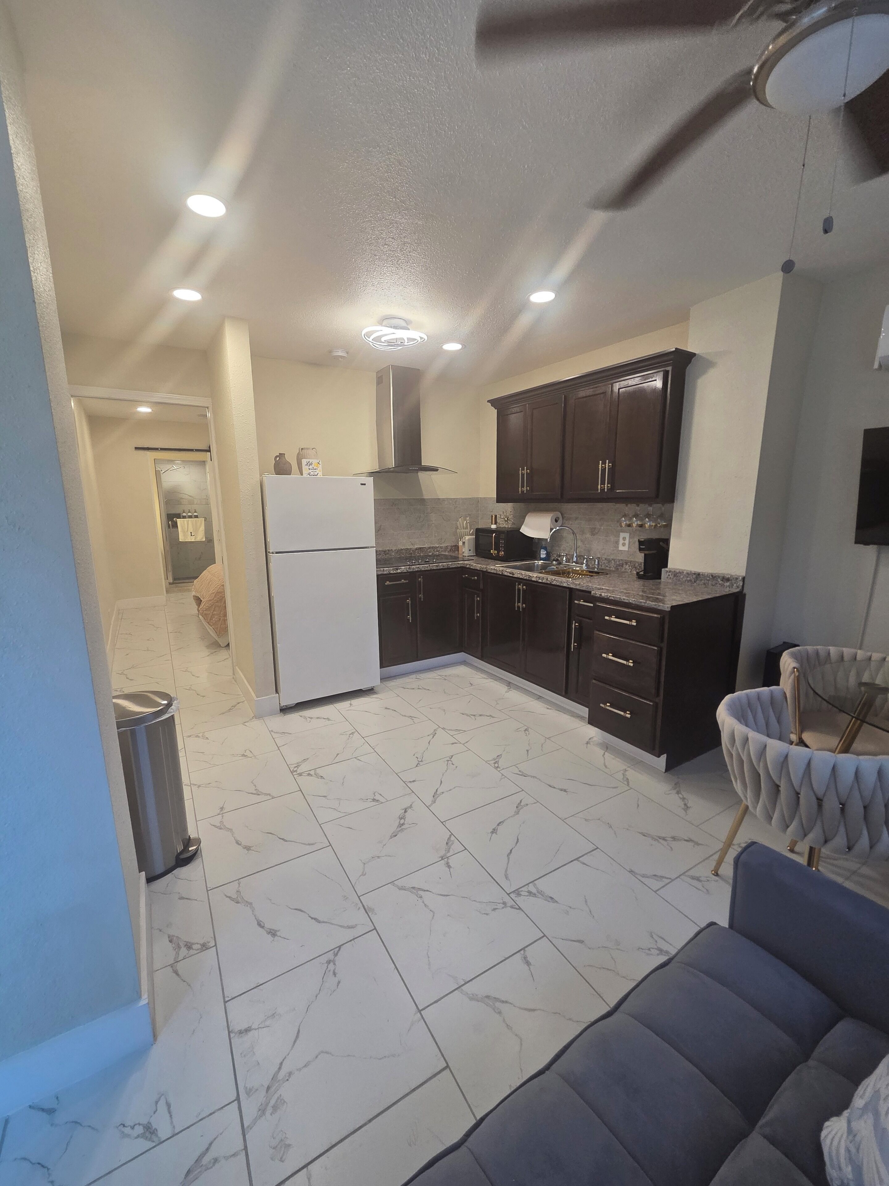 A modern kitchen with dark cabinets, a white refrigerator, and a marble-tiled floor.