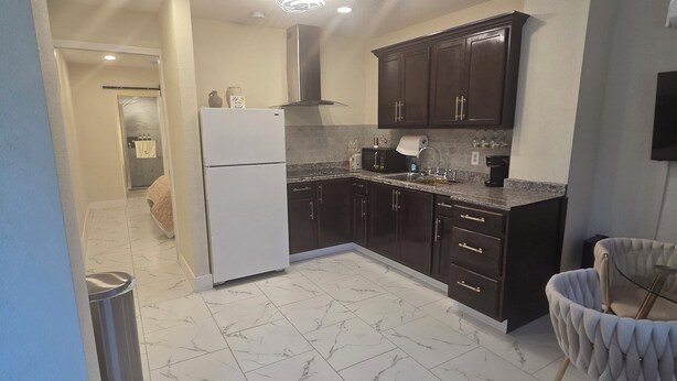 Uma cozinha moderna com armários escuros, uma geladeira branca e piso de mármore.