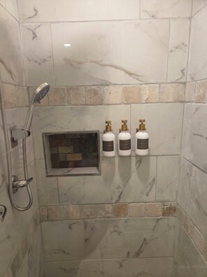 Ein Duschbereich mit Handbrause, einem durch eine Glasscheibe abgetrennten Fenster und drei Toilettenartikeln.