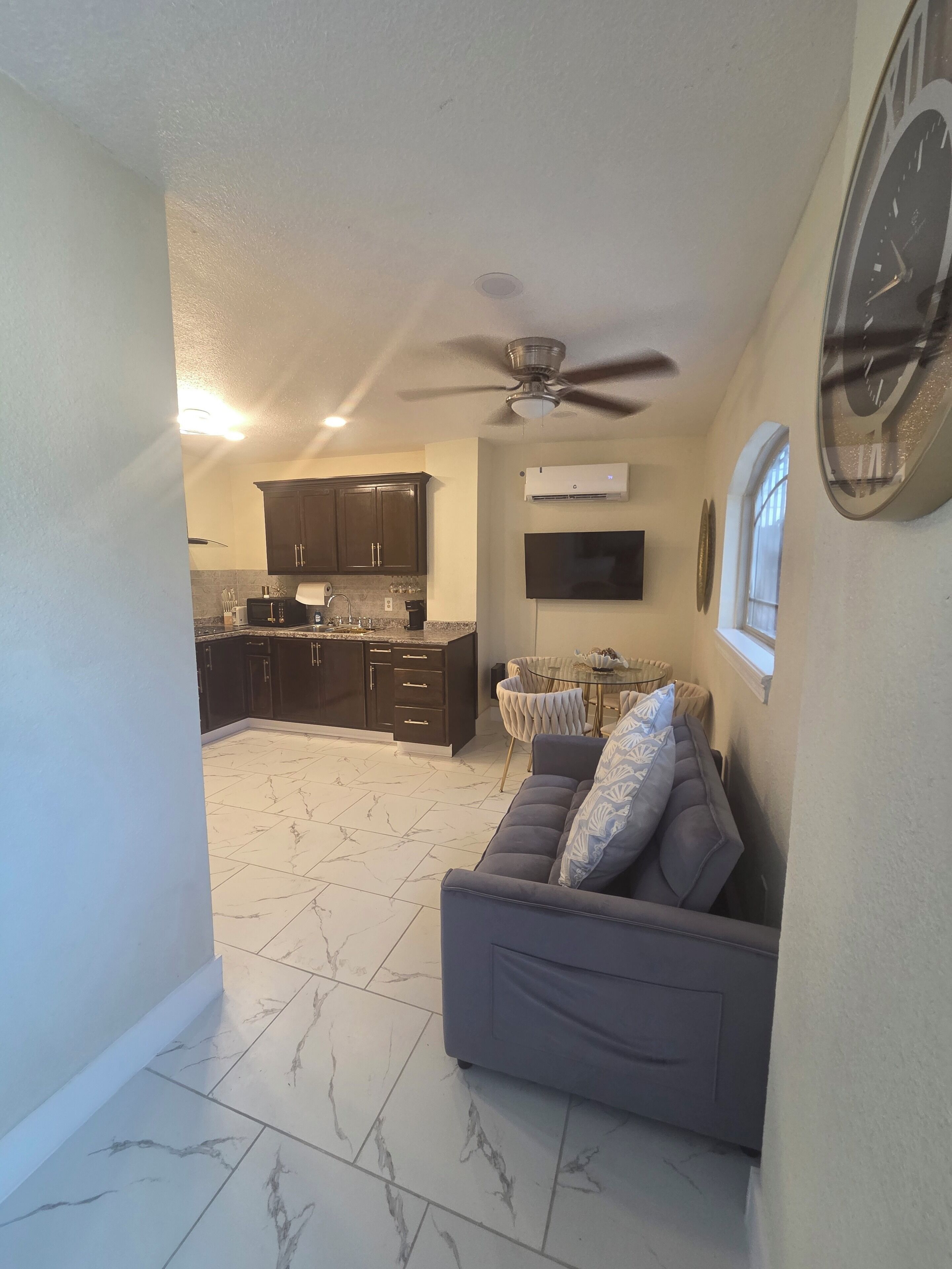 A modern kitchen with dark cabinets, a dining area with a round table, and a grey sofa.
